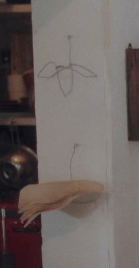 Two wire hangers mounted on the wall, shaped to function as shelves. One is holding pieces of paper.